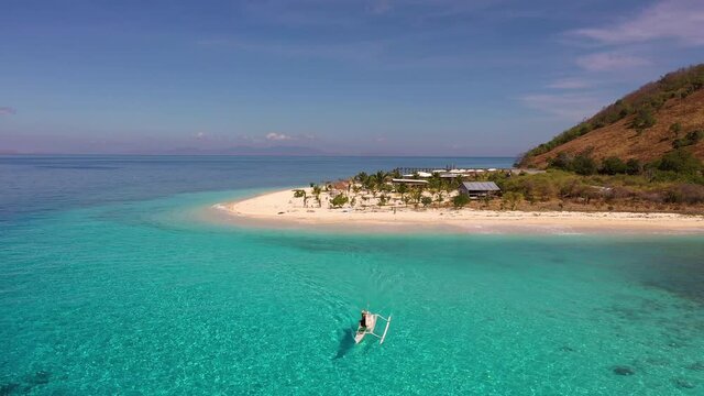 Aerial drone footage of fisherman boat sailing off the turquoise waters of an idyllic island off the coast of Flores in Labuan Bajo, Indonesia. Shot with a backward motion. 