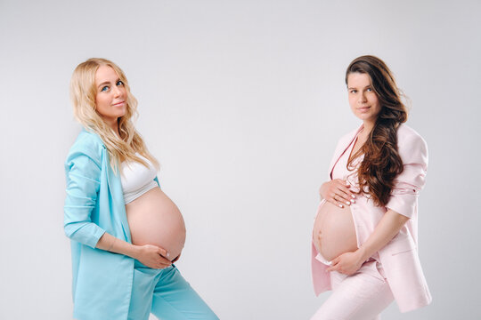 Two pregnant women with big bellies in suits on a gray background