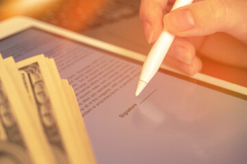 Signing the contact with electronic signature on the tablet. Business success concept with money