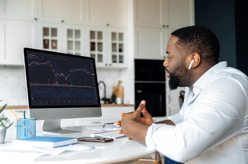 Investments, trading on the stock exchange. African american man trader investor, is analysing cryptocurrency financial market, looks at computer,trading data index chart graph on pc screen