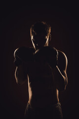 Fototapeta na wymiar Silhouette of a fighter in boxing gloves. Portrait on a dark background. vertically