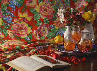 mesa com jarra de chá, copos, vasos com flores e livro aberto com pétalas ao lado