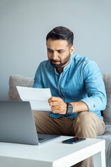 Portrait of concentrated indian businessman with laptop reading contract