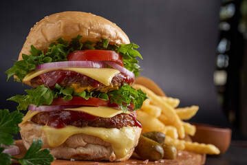 Homemade hamburger or burger with fresh vegetables and cheese lettuce and mayonnaise served, French fries on pieces of brown paper on black stone table . concept of fast food and junk food