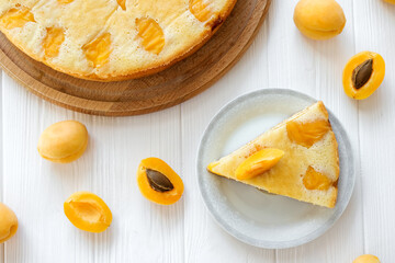 Piece of apricot pie on plate with full cake and apricot fruits on white table. Easy recipe of summer cake for tea time. Homemade bakery of holiday snack by classic recipe. Shortbread bakery. Flat lay
