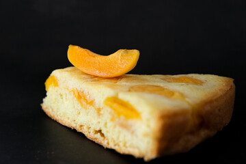 Obraz na płótnie Canvas Piece of shortcrust apricot pie with slice of apricot fruit on black background. Delicious recipe of summer fruit biscuit. Luxury dessert cake, cafe menu. Minimalism in food photo.