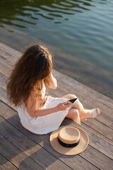 Fototapeta na wymiar woman sitting on the pier and texting, holding mobile phone