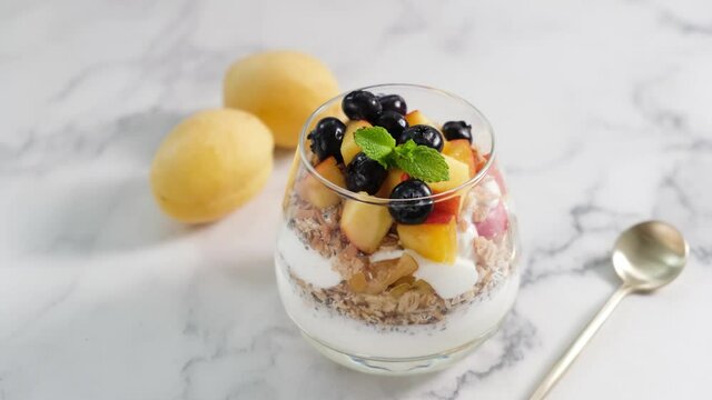 Yogurt and granola parfait with fruits and berries in a glass jar on white marble table background. Healthy food