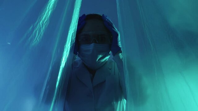 Pandemic outbreak. Disaster area. Health risk. Medical horror. Scared terrified female doctor in ppe face mask running away from blue pink neon smoke lab tent isolation.