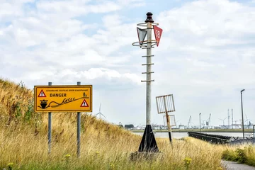 Foto op Plexiglas View of the Nieuwe Waterweg in Hoek van Holland, with a warning sign for dangerous waves. Across the street one of the ports of Rotterdam. Netherlands, Holland, Europe © Gina