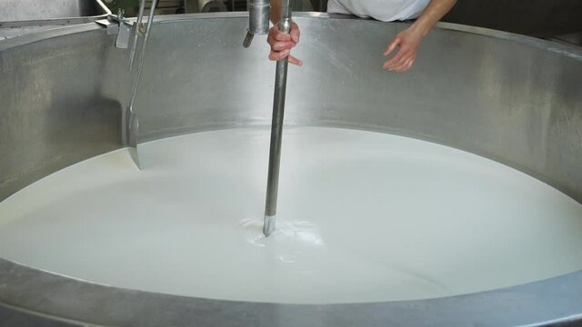 Worker hands remove stirring blade from stainless steel reservoir in a small dairy and cheese making factory - close up