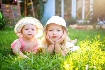 two children girls sisters on a green lawn in the summer in the sun in hats
