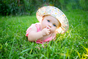 cute baby girl on a green lawn in summer in the sun wearing a hat