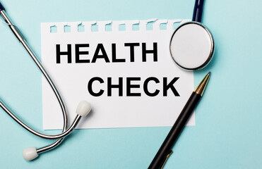 On a light blue background, a stethoscope, a pen and a sheet of paper with the inscription HEALTH CHECK. Medical concept