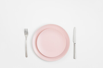 Empty pink plate and silver cutlery on a white background. Minimal table setting. Mockup or template. View from above. Copy space.