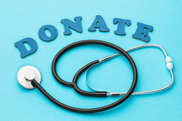 Word from wooden letters and medical stethoscope on blue background, concept on the topic of donation for treatment