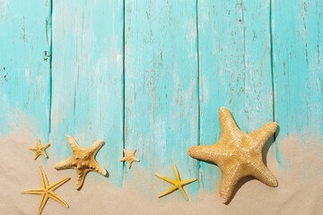 Flat composition with various starfish on a blue wooden background with sand and copy space at the top