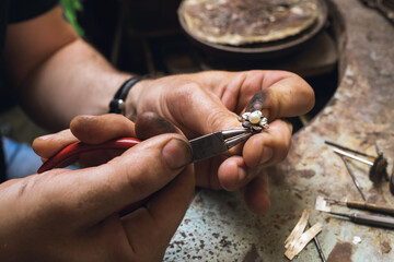 A jeweler disassembles a gold ring with pearls in a workshop, close-up