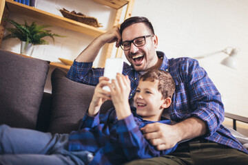 Father and son are using smartphones play video game and smiling while spending time together at home