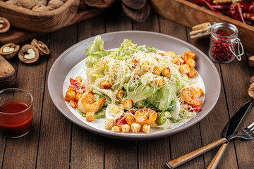 Plate of caesar salad with shrimp and lettuce on wooden background