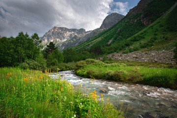 Fototapeta na wymiar A beautiful alpine gorge of the Ullu-Murudzhu River with green meadows and mountain peaks in the Karachay-Cherkess Republic