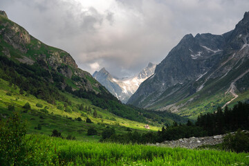 Fototapeta premium A beautiful alpine gorge of the Ullu-Murudzhu River with green meadows and mountain peaks in the Karachay-Cherkess Republic