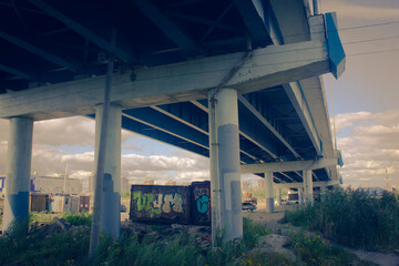 the space under the bridge, a neglected place with graffiti and debris, concrete columns support the flyover