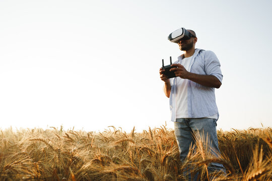 Young man standing in a wheat field at sunset in virtual reality glasses - Powered by Adobe