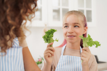 Mother and daughter playing and having fun with vegetables in kitchen