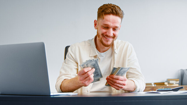 Smiling self employed businessman counts cash income holding dollar banknotes