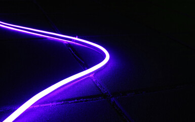Purple led neon flexible strip light illuminated on the floor in dark light.