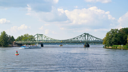 Die Glienicker Brücke über den Fluss Havel zwischen Potsdam und Berlin. Im Vordergrund ein Ausflugsschiff mit Touristen.