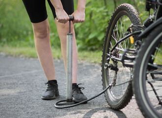 A girl pumps a bicycle wheel with a pump. Bicycle repair in the forest. Close up