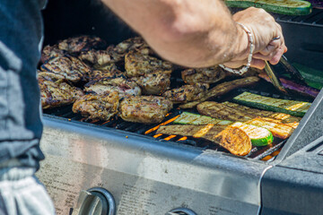 Close view of male hand handling meat and vegetables with tongs on the hot grill of a barbecue set