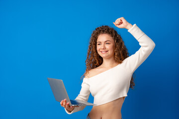 Young curly-haired woman holding laptop against blue background
