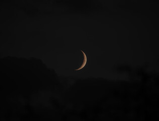 Waxing Crescent moon in a rich golden colour sitting just above some ominous clouds