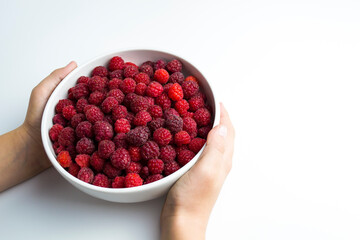 A close-up shot of a fresh raspberry in a white cup a child is holding in his hands - ideal for a culinary blog diet and the benefits of natural vitamins for children is a replacement for medications