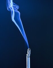 Burning cigarette with wisp of smoke dark background, smoking