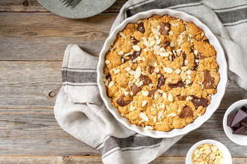 Homemade shortbread pie with milk and bitter chocolate in a baking dish on a gray wooden culinary background top view from a copyspace. Delicious rustic sweet pastries
