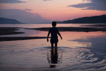 Fototapeta premium happy kid walking along the mirror water enjoying the evening fiery sunset 