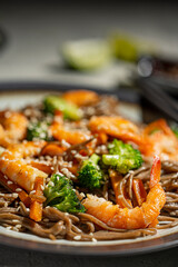 Buckwheat noodles with shrimps, carrots, broccoli, green onions and soy sauce. Vegan soba noodles. Asian food on grey textured table. Seafood healthy diet concept, copy space. 