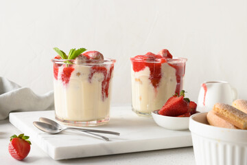 Layered dessert in glass jars with cookies savoyardi, mascarpone and whipped cream decorated strawberries. Italian tiramisu with summer vibes on white.