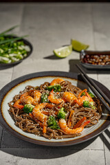 Buckwheat noodles with shrimps, carrots, broccoli, green onions and soy sauce. Vegan soba noodles. Asian food on grey textured table. Seafood healthy diet concept, copy space. 