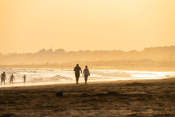 sunset on the beach of huelva with silhouettes of people - obrazy, fototapety, plakaty
