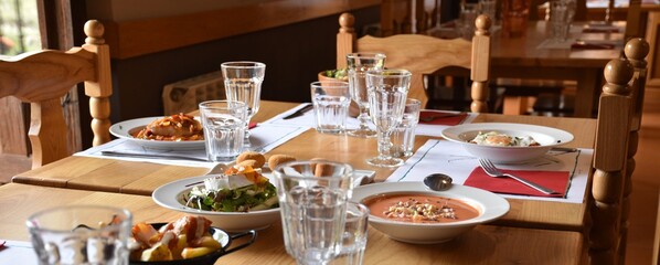 Restaurant with different dishes of food and servings served. Wooden furniture, natural light, pleasant atmosphere.