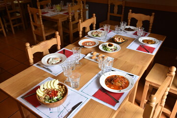Table in restaurant with different dishes of food served. Wooden tables and chairs, intimate atmosphere without people.