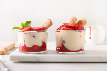 Layered summer dessert in glass jars with cookie savoyardi, mascarpone and whipped cream decorated strawberries. Close up. Italian tiramisu with summer vibes on white.