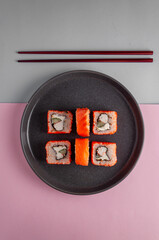 Sushi on a gray dish with Chinese chopsticks on a gray and pink background, minimalism, top view
