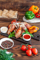 Barbecue with spices and herbs on a wooden brown background, with basil, sauce, pepper and tomatoes