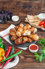 Grilled chicken on a wooden board, with hot pepper, vegetables and sauce, with juicy basil and tarragon on a brown wooden background